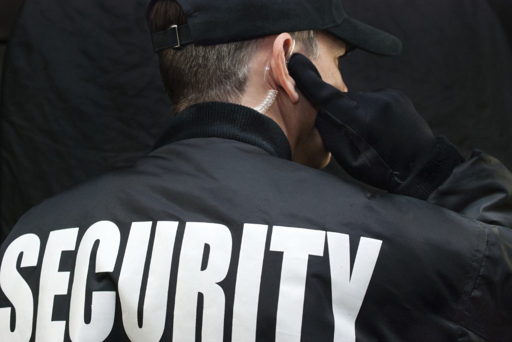 Security Guard Listens To Earpiece, Back of Jacket Showing - HospitalityLawyer.com®