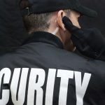 Security Guard Listens To Earpiece, Back of Jacket Showing - HospitalityLawyer.com®