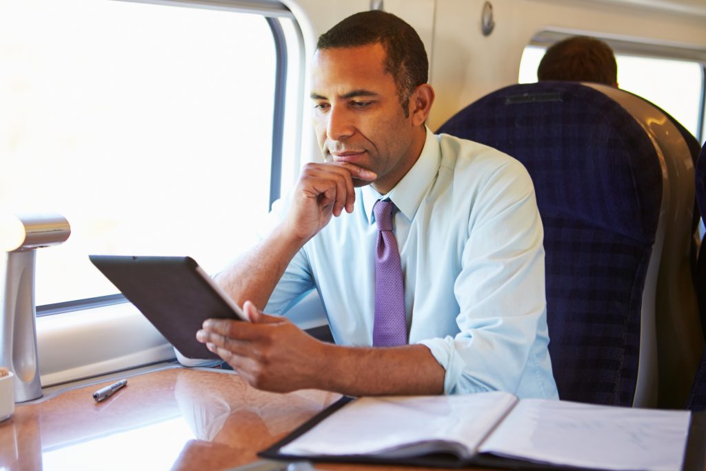 Businessman Commuting On Train Using Digital Tablet - HospitalityLawyer.com®