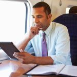 Businessman Commuting On Train Using Digital Tablet - HospitalityLawyer.com®
