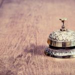 Vintage bronze hotel reception service desk bell on wooden table background. Old retro style filtered photo - HospitalityLawyer.com®