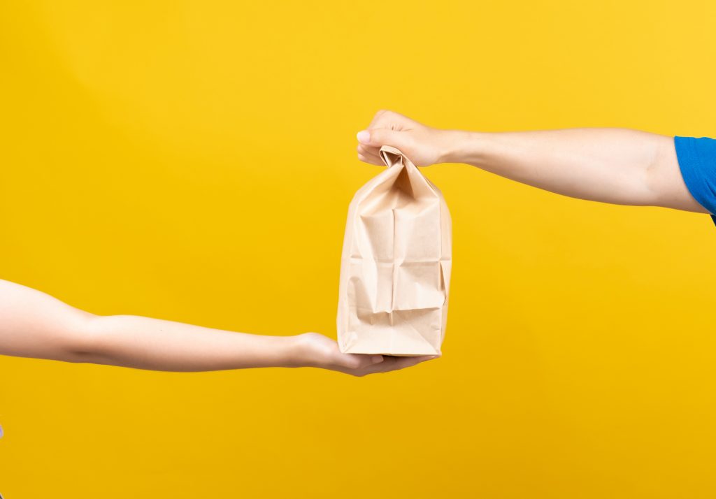 Hand to hand of Delivery food service sending delicious from restaurant to customer without having to leave the house receiver shipping deliver shopping online on yellow background isolated. - HospitalityLawyer.com®