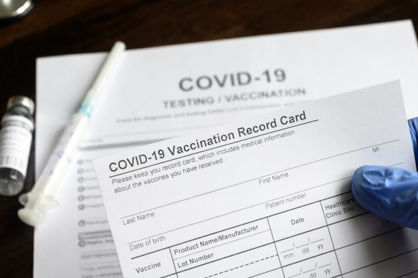 COVID-19 Vaccination Record Card in doctor hand, coronavirus test and vaccine medical form on desk in clinic. Concept of corona virus vaccination certificate, health passport and immunization.