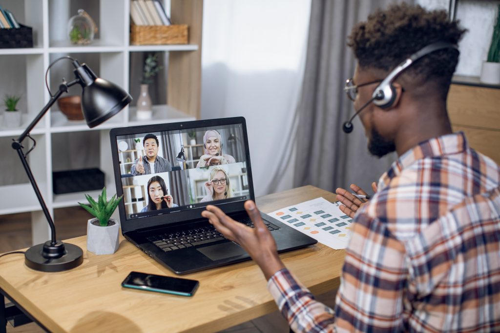 Multiethnic group of people having online working meeting - HospitalityLawyer.com® Multiethnic group of people having business meeting through video call on laptop. View from shoulder of black man sitting at home office and working remotely.