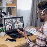 Multiethnic group of people having online working meeting - HospitalityLawyer.com® Multiethnic group of people having business meeting through video call on laptop. View from shoulder of black man sitting at home office and working remotely.