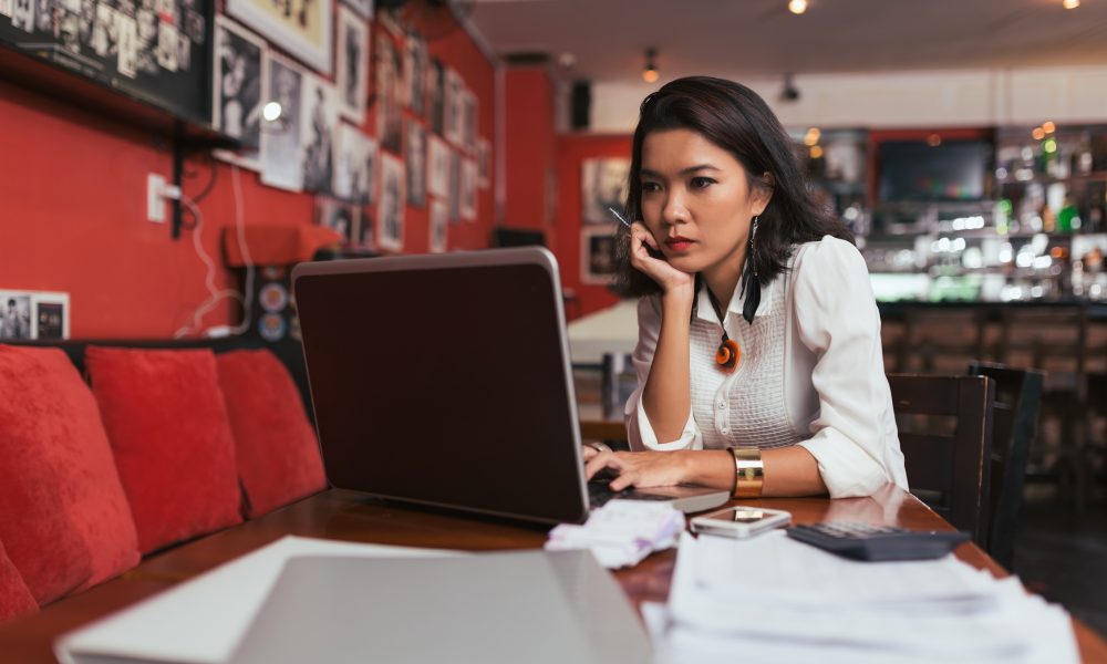 Pensive Asian bar owner using laptop to pay bills online