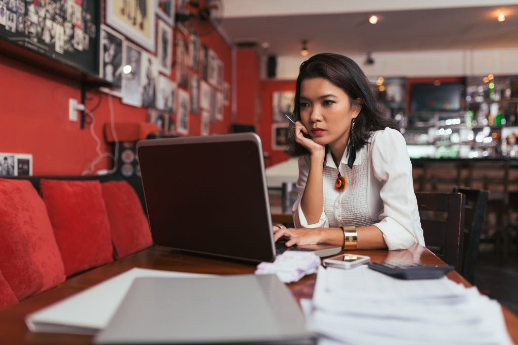 Paying bills online - HospitalityLawyer.com® Pensive Asian bar owner using laptop to pay bills online