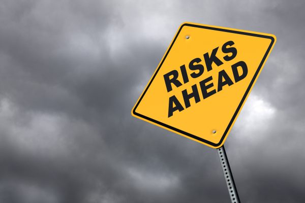 A yellow road sign warning of the risks ahead. Perspective is from a low camera angle against an ominous gray sky background. Road sign is placed on right side of image allowing for copy space on the left side of image.
