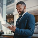 Businessman, digital tablet or strategy planning in hotel conference lobby or airport travel lounge. Happy smile, corporate worker or technology app to budget company finance or schedule target goals
