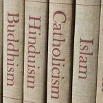 Book spines listing major world religions - Judaism, Islam, Catholicism, Hinduism, Buddhism and Protestantism.