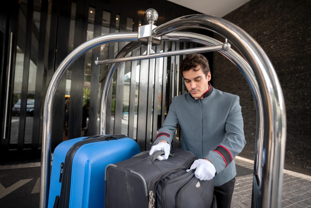 Focused male bellhop placing bags on luggage cart for a guest check in - HospitalityLawyer.com® Focused male bellhop placing bags on luggage cart for a guest check in
