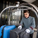 Focused male bellhop placing bags on luggage cart for a guest check in - HospitalityLawyer.com® Focused male bellhop placing bags on luggage cart for a guest check in