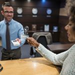 Woman paying with bank card in the hotel - HospitalityLawyer.com® Young Caribbean woman paying at the reception desk as checking out