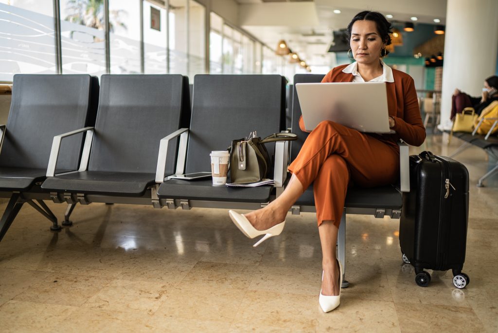 Businesswoman using laptop in the departure area at airport - HospitalityLawyer.com® Businesswoman using laptop in the departure area at airport