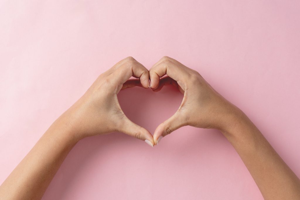 Heart shape created from young womans hands on pastel pink background - HospitalityLawyer.com®