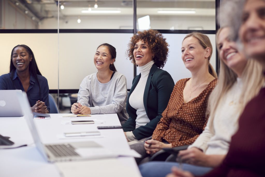 Line Of Businesswomen In Modern Office Listening To Presentation By Colleague - HospitalityLawyer.com®