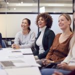 Line Of Businesswomen In Modern Office Listening To Presentation By Colleague - HospitalityLawyer.com®