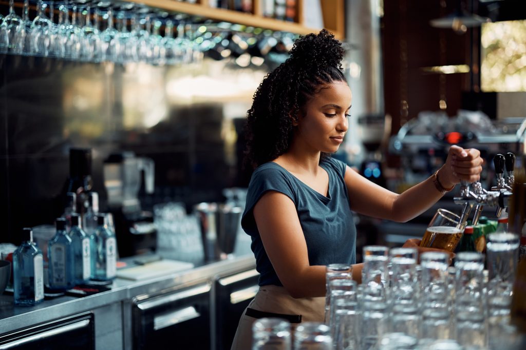 waitress pouring beer draft beer while working at bar counter - HospitalityLawyer.com®