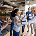 Boss giving woman a promotion at the office and team clapping for her - HospitalityLawyer.com®
