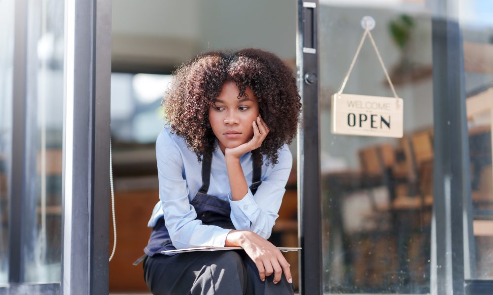 Female shopkeeper sitting stressed out at the store entrance frustrated