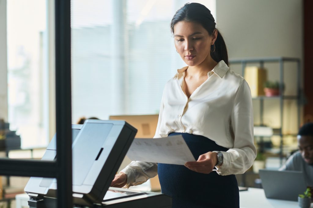 Young pregnant secretary using xerox - HospitalityLawyer.com®