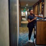 Black female housekeeper replenishing toiletries in guest rooms in a hotel - HospitalityLawyer.com® Black female housekeeper replenishing toiletries in guest rooms in a hotel