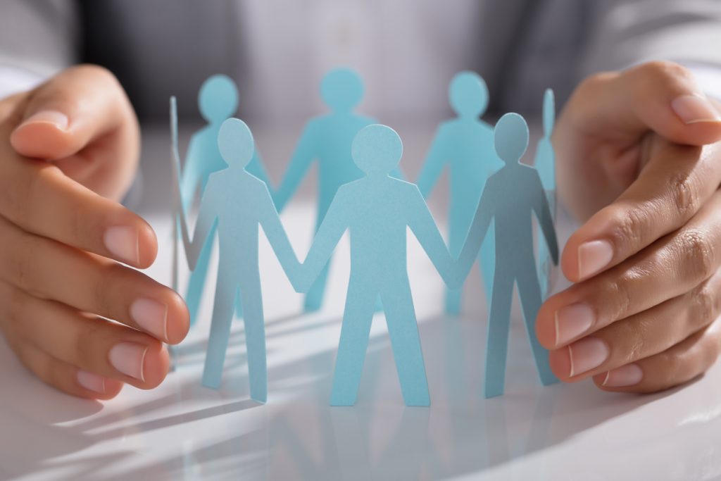 Businessperson Hand Protecting Paper Cut Out Figure On Table - HospitalityLawyer.com®