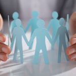 Businessperson Hand Protecting Paper Cut Out Figure On Table - HospitalityLawyer.com®