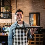 Portrait of waiter carrying a finished dish in a restaurant - HospitalityLawyer.com®