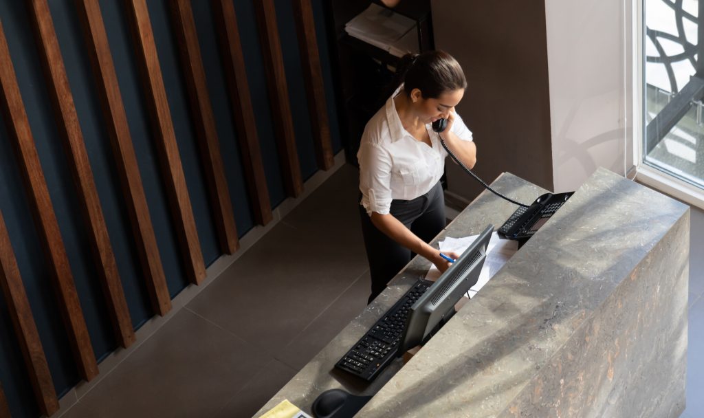 Latin american hotel receptionist taking a phonecall - HospitalityLawyer.com®