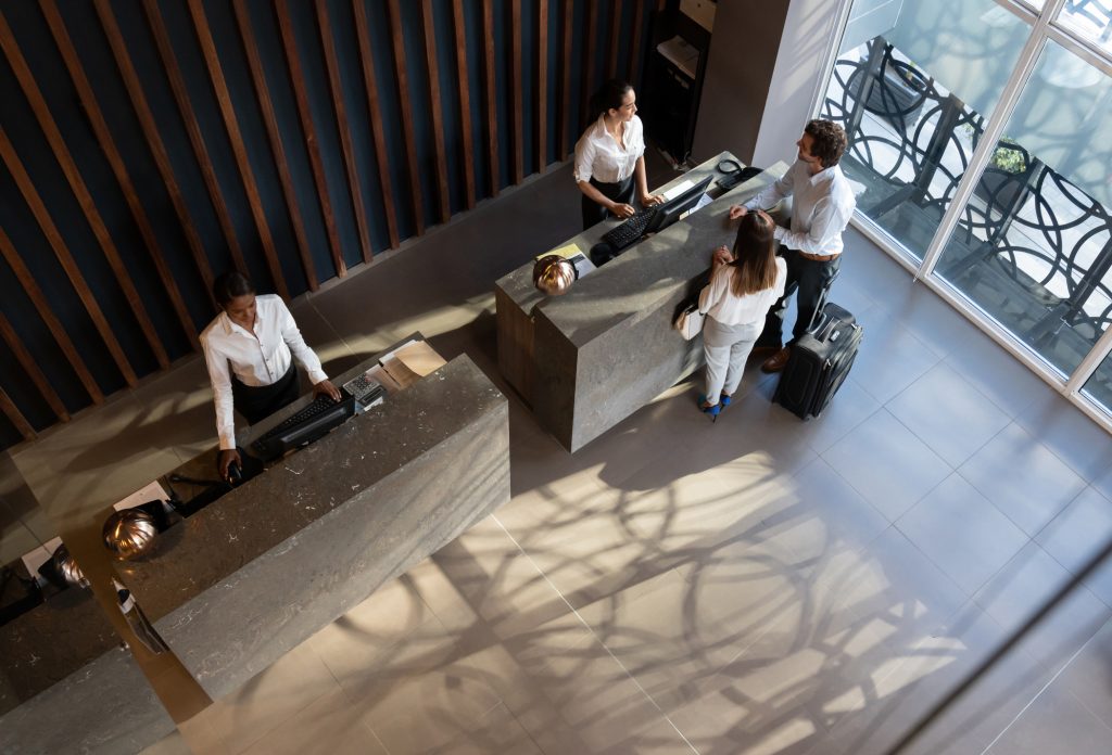 Young business couple checking in at hotel and beautiful receptionist helping them - HospitalityLawyer.com®