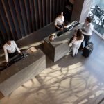 Young business couple checking in at hotel and beautiful receptionist helping them - HospitalityLawyer.com®